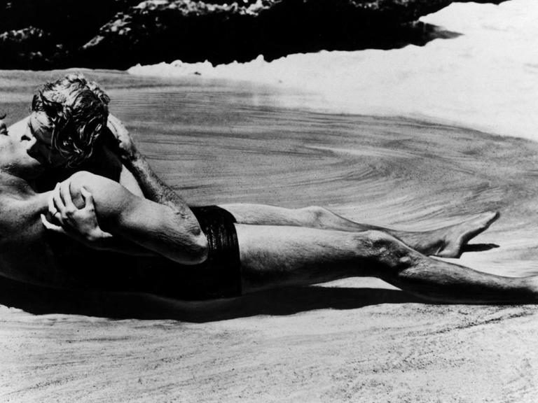 Ein Film-Still zeigt die Schauspielerin Deborah Kerr und Filmpartner Burt Lancaster bei einem Kuss am Strand von Hawaii von einer Welle umspült