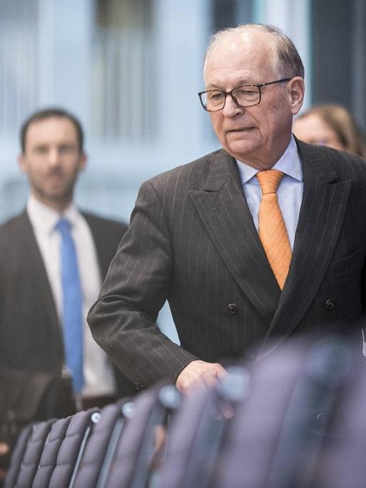Wolfgang Ischinger im Rahmen einer Pressekonferenz in Berlin. Er geht an einer Stuhlreihe vorbei. Ernster Gesichtsausdruck, Nadelstreifenanzug, hellblaues Hemd und orangene Krawatte.