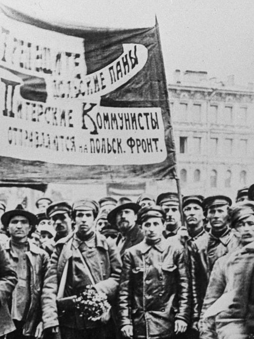 Ein Schwarzweiß-Foto zeigt etwa ein Dutzend Männer, teils in Uniform zumeist in Lederjacken und mit Schirmmützen ein großes, kyrillisch beschriebenes Banner hochhaltend