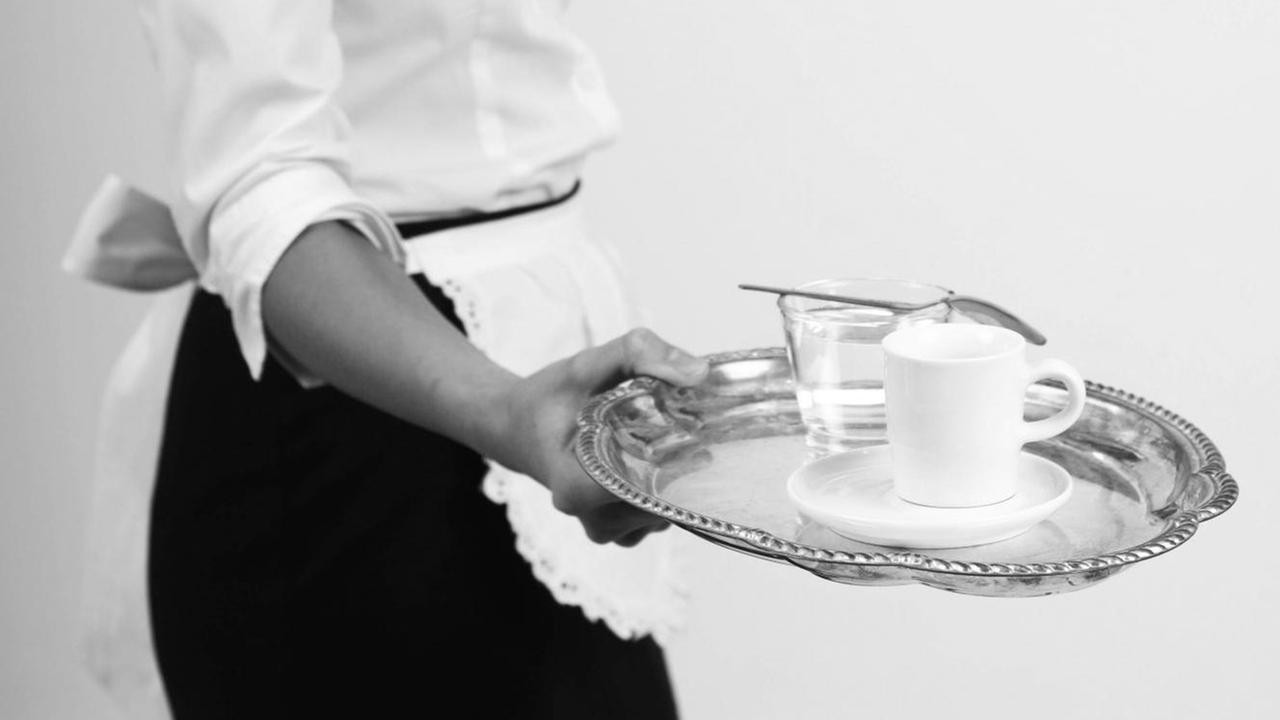 Eine Kellnerin in einer weissen Schürze serviert Espresso auf einem Silbertablett.