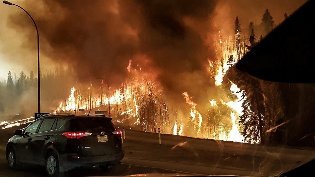 Brennender Wald, im Vordergrund ein Auto und ein Gebäude.