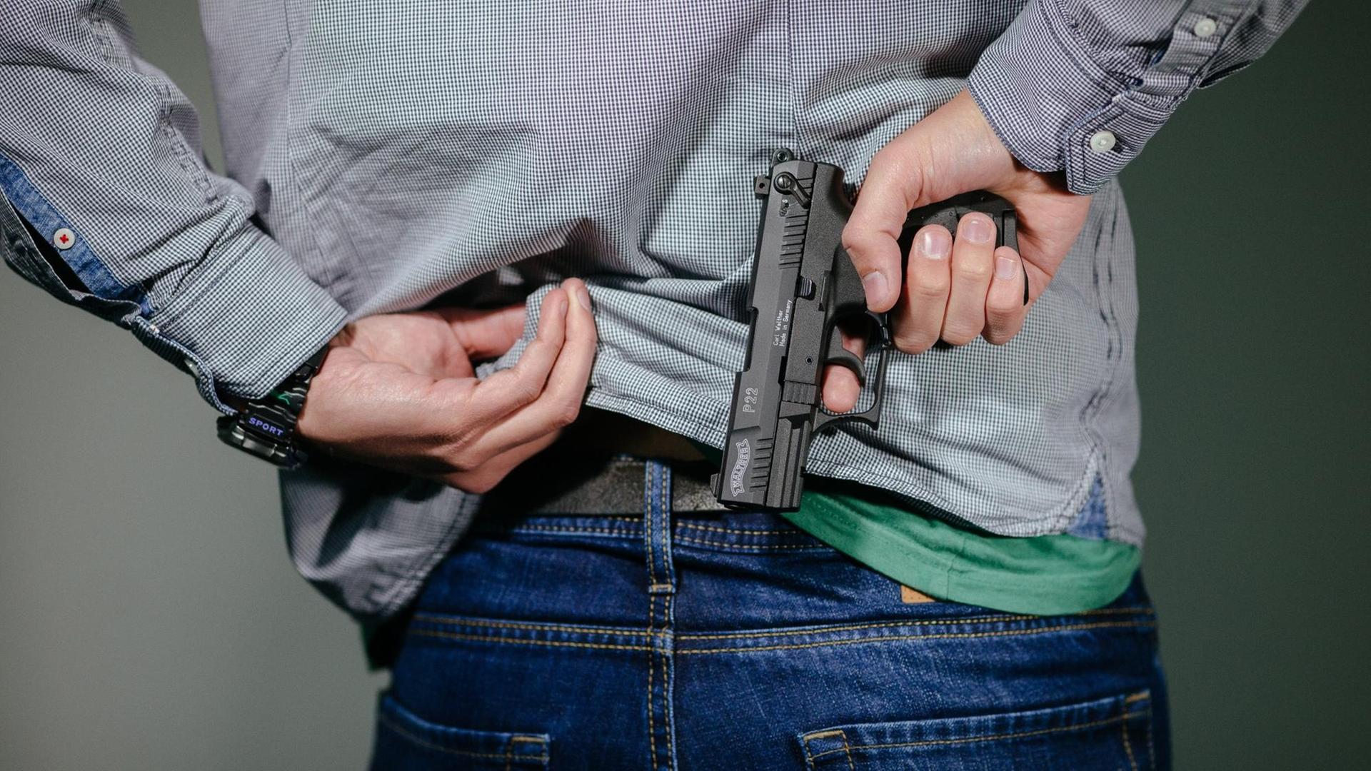 Ein Mann steckt sich eine Schreckschuss-Pistole "Walther P22" in den Hosenbund.