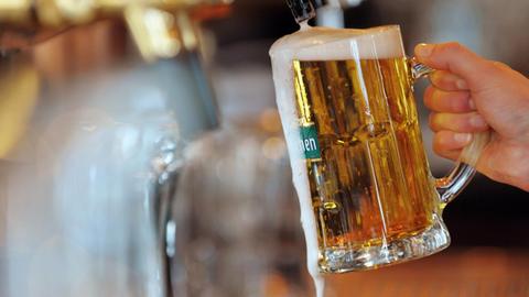 Eine Hand hält ein mit Bier gefülltes Glas unter einen Zapfhahn.