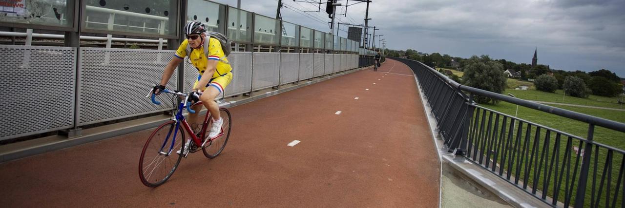 Ein Mann in gelbem Radfahrtrikot fährt auf einer rot asphaltierten Brücke auf einem gut ausgebauten Radweg. Ein Mann in gelbem Radfahrtrikot fährt auf einer rot asphaltierten Brücke auf einem gut ausgebauten Radweg.