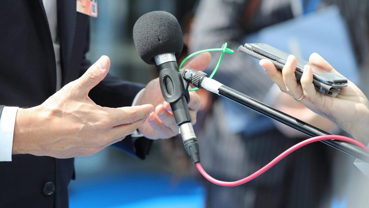 Ein Mikrofon, ein Smartphone und Hände sind in einer Nahaufnahme zu sehen.