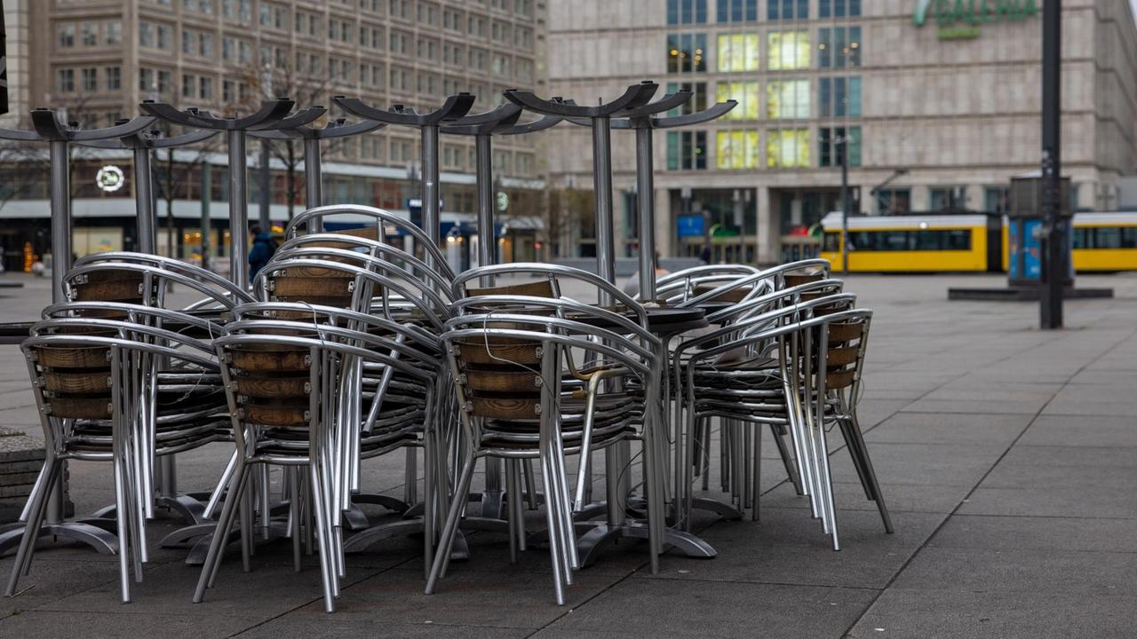 Auf dem Berliner Alexanderplatz sind Tische und Stühle eines Restaurants gestapelt und zusammengestellt.
