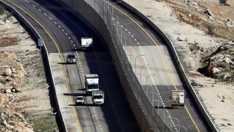 Autos fahren auf einer neuen israelischen Straße, die durch eine Mauer geteilt ist