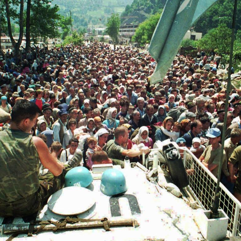 Niederländische UN-Blauhelm-Soldaten sitzen auf einem Panzer in der Nähe des Dorfes Potocari am 13. Juli 1995. Vor ihnen bosnische Flüchtlinge