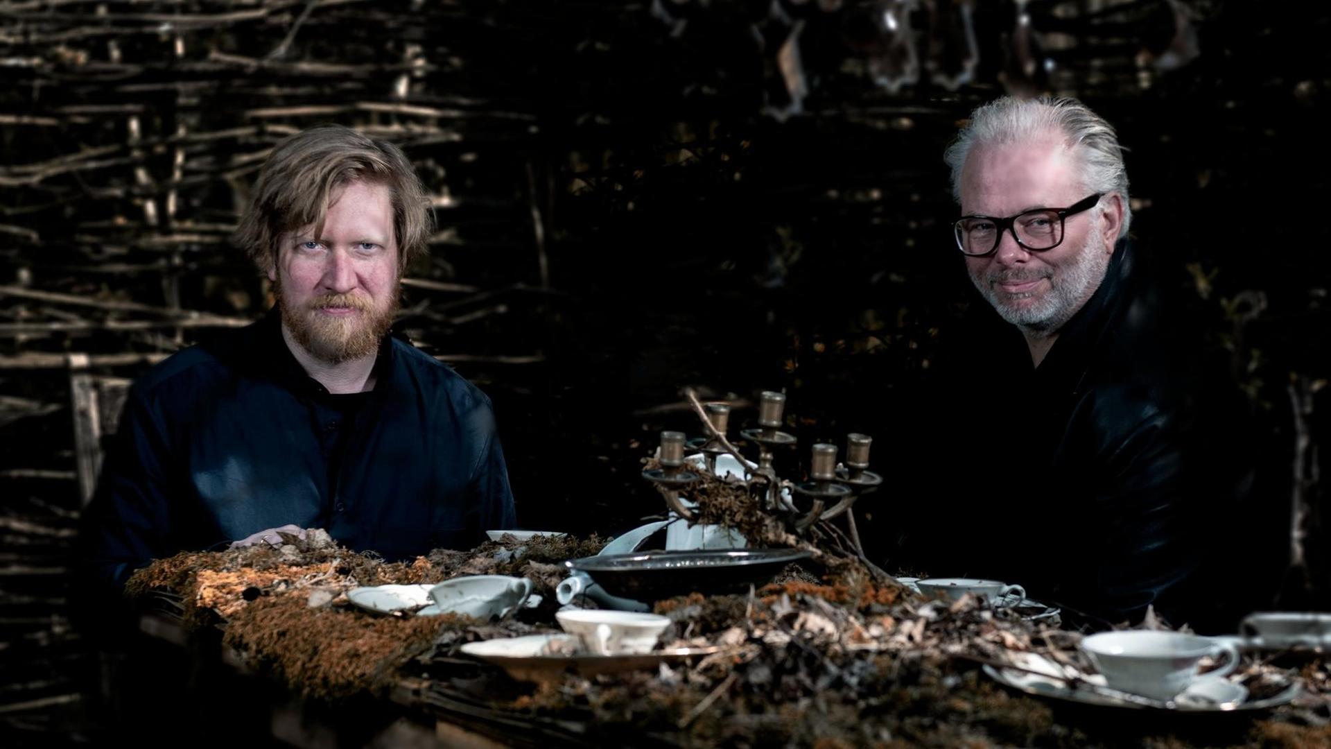 Knut Hem & Helge Lien sitzen gemeinsam am Tisch mit Walddekoration