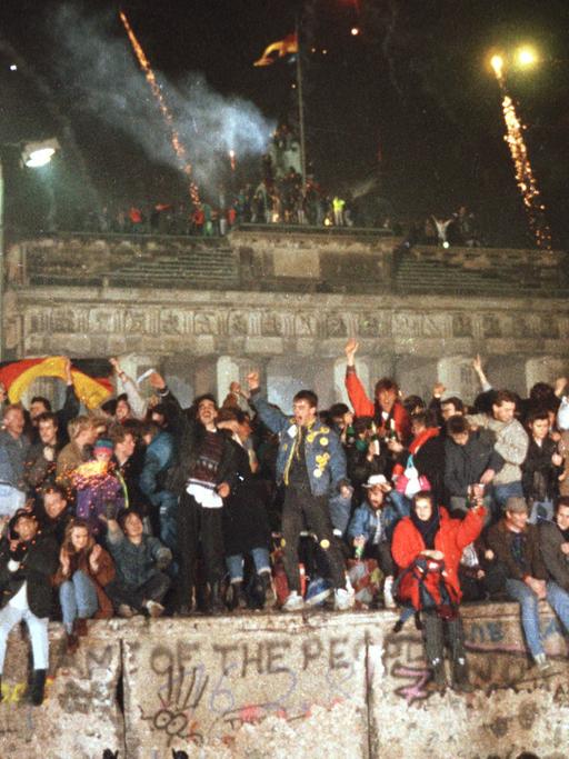 Ausgelassen feiern Menschen am 31.12.1989 auf der Berliner Mauer vor dem Brandenburger Tor.