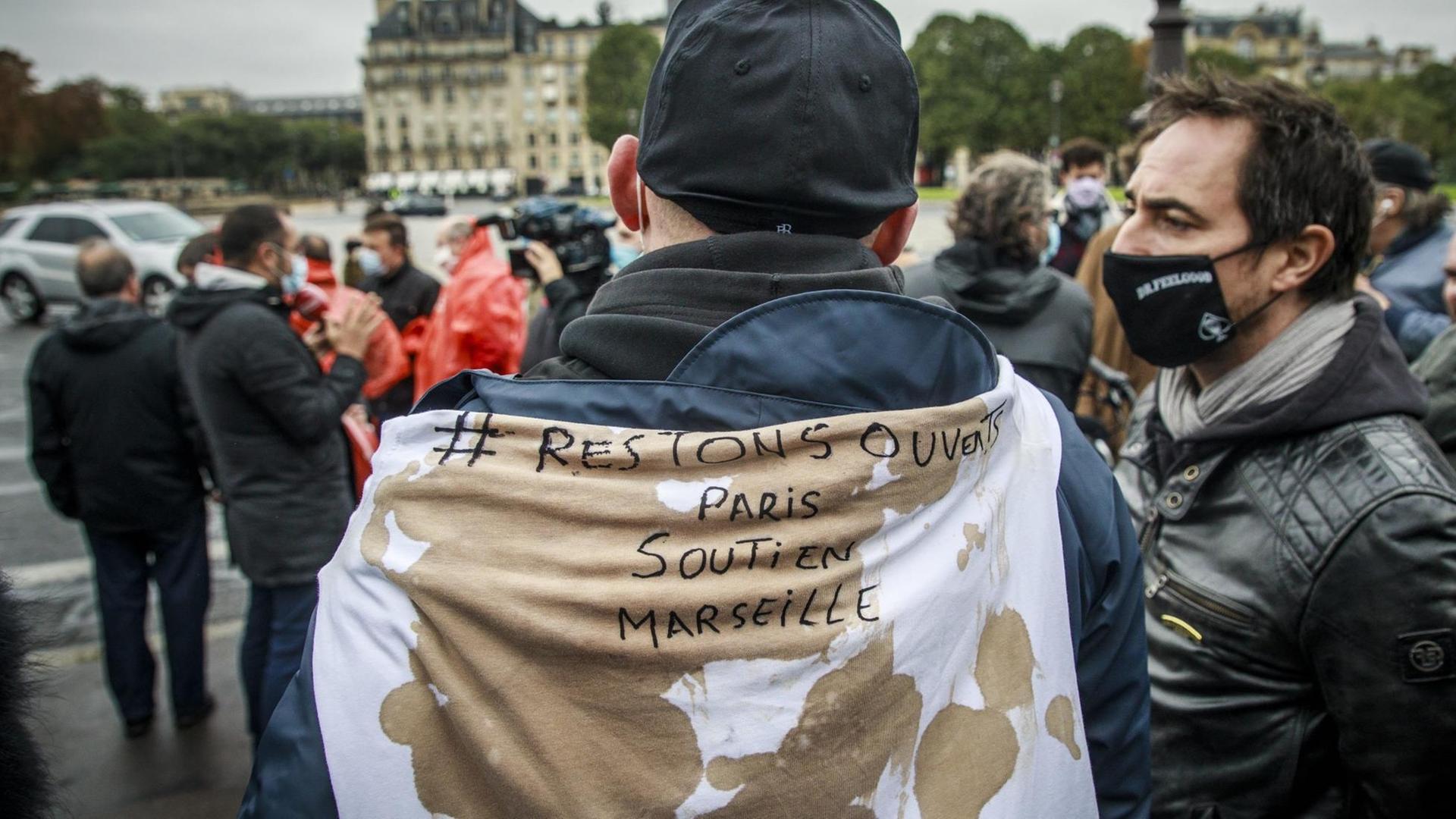 Ein Mann hat sich ein Spruchband mit der Aufschrift "Restons ouverts - Paris soutin Marseilles" umgehängt ("Bleiben wir offen - Paris unterstützt Marseille")
