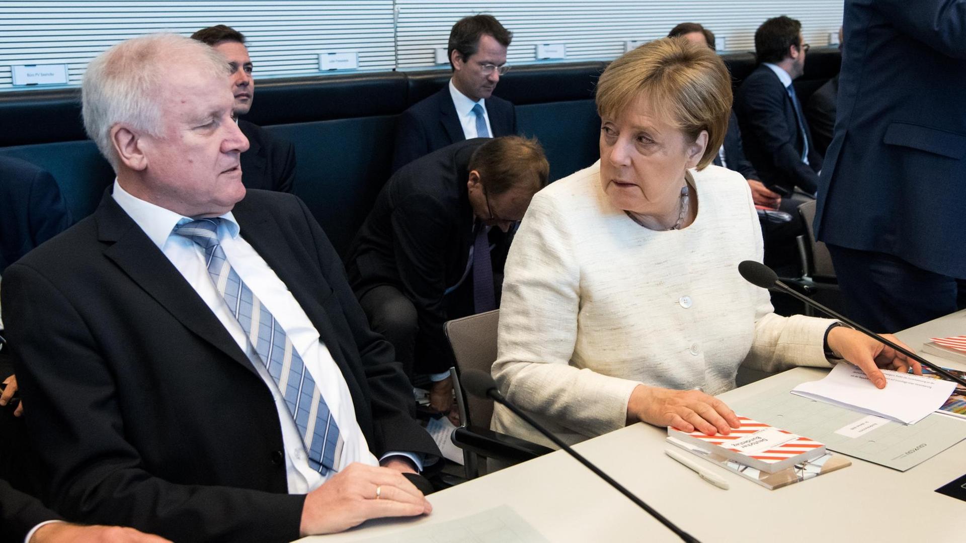 Seehofer (l) und Merkel (r) sitzen nebeneinander an einem Tisch und tauschen distanzierte Blicke.