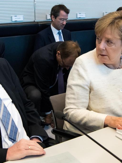 Seehofer (l) und Merkel (r) sitzen nebeneinander an einem Tisch und tauschen distanzierte Blicke.