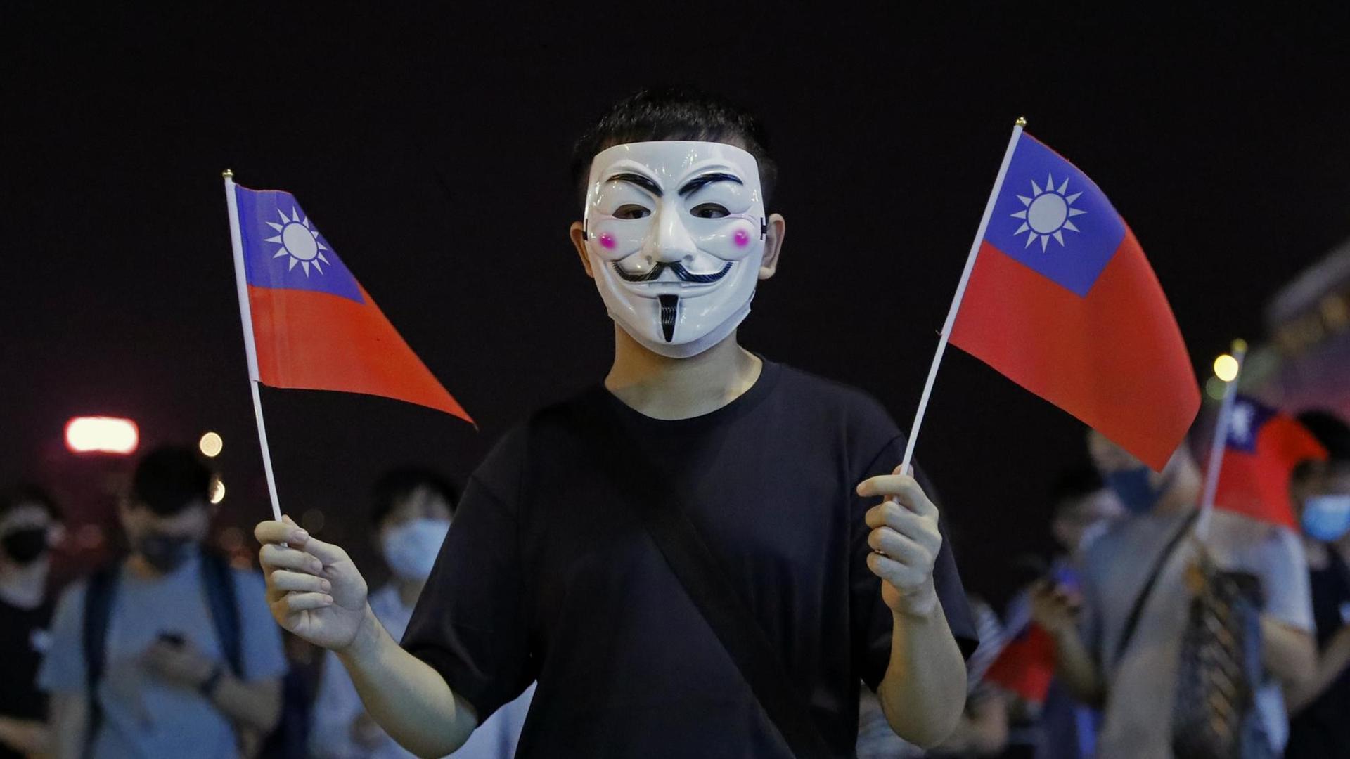 Ein Mann mit Maske hält bei einer Kundgebung für die Unabhängigkeit Taiwans am National Day Taiwans am 10.10.2019 zwei taiwanesische Flaggen.