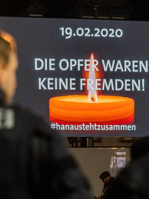 Polizisten stehen auf dem Hanauer Marktplatz, wo auf einer Videoleinwand die Trauerfeier für die Opfer der rassistischen Morde übertragen wird.