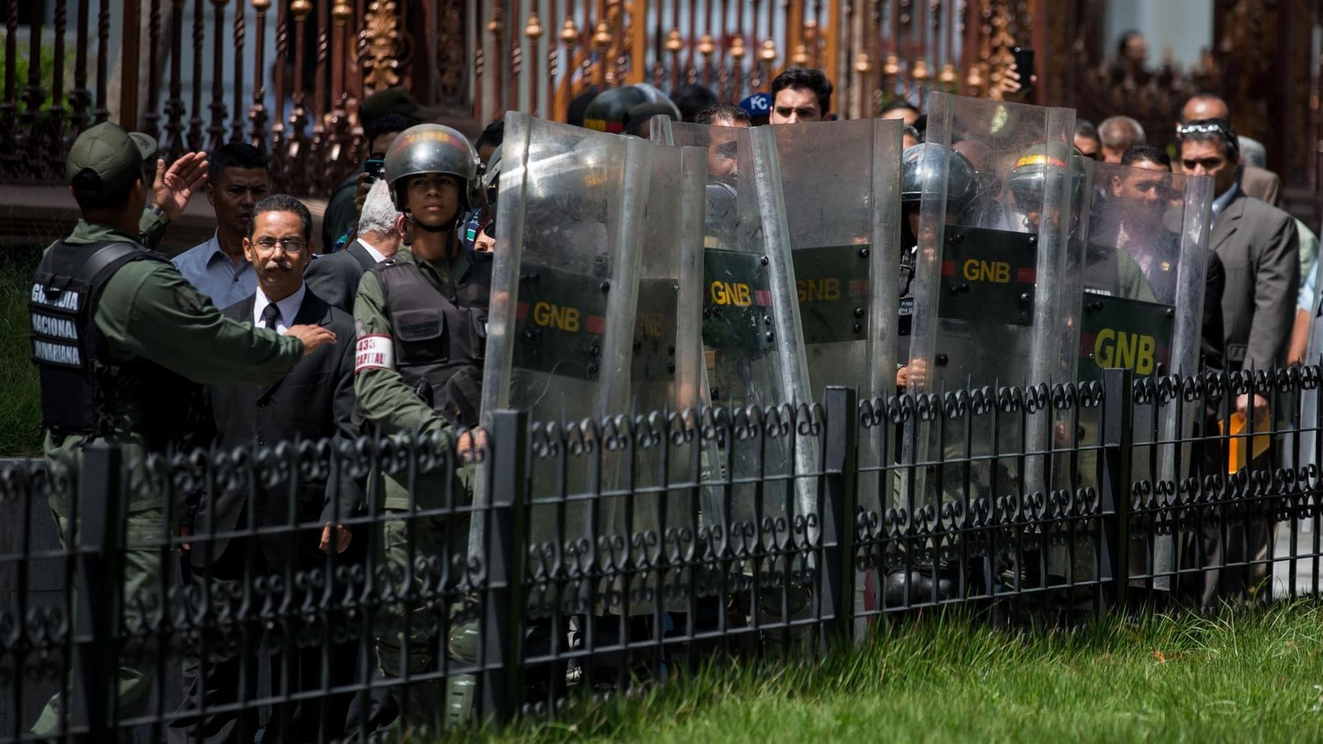 Streitkräfte Boliviens in Caracas (Venezuela) stehen an einem Zaun. Sie tragen Schutzschilde.