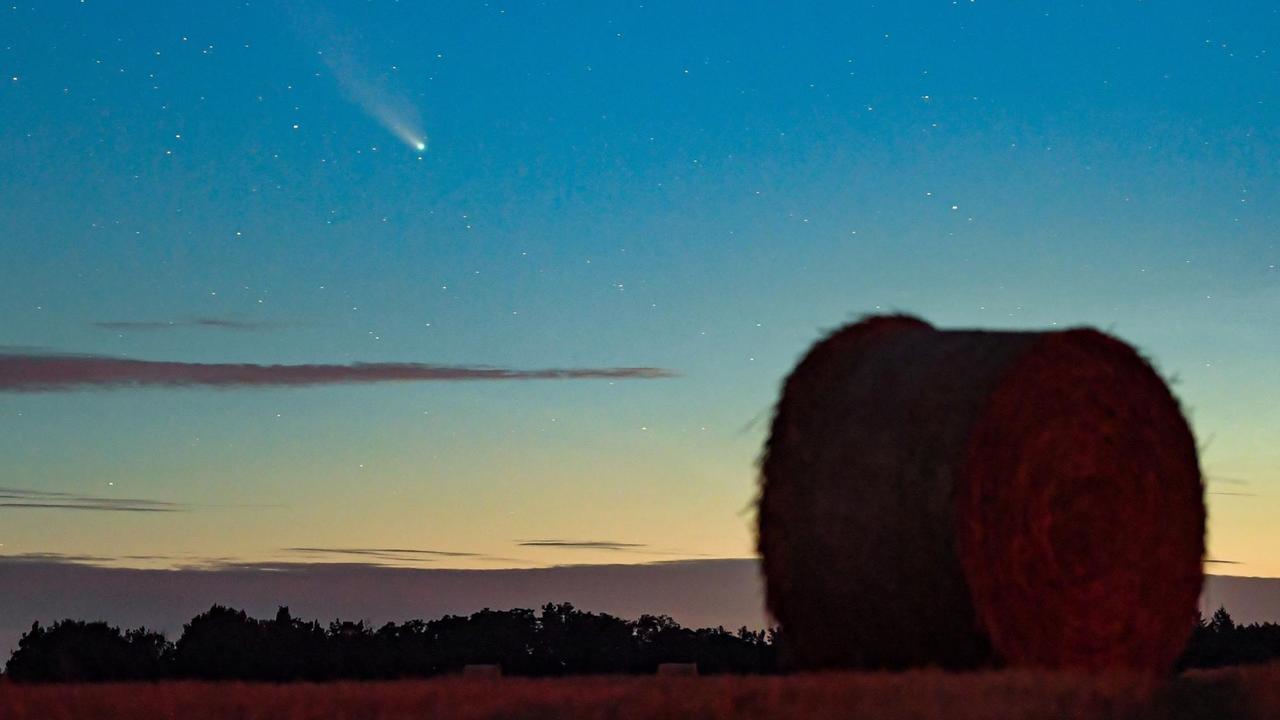 Der Komet Neowise, auch C/2020 F3 genannt, leuchtet am zeitigen Morgenhimmel gegen 3 Uhr über einem Feld mit einer Strohrolle.