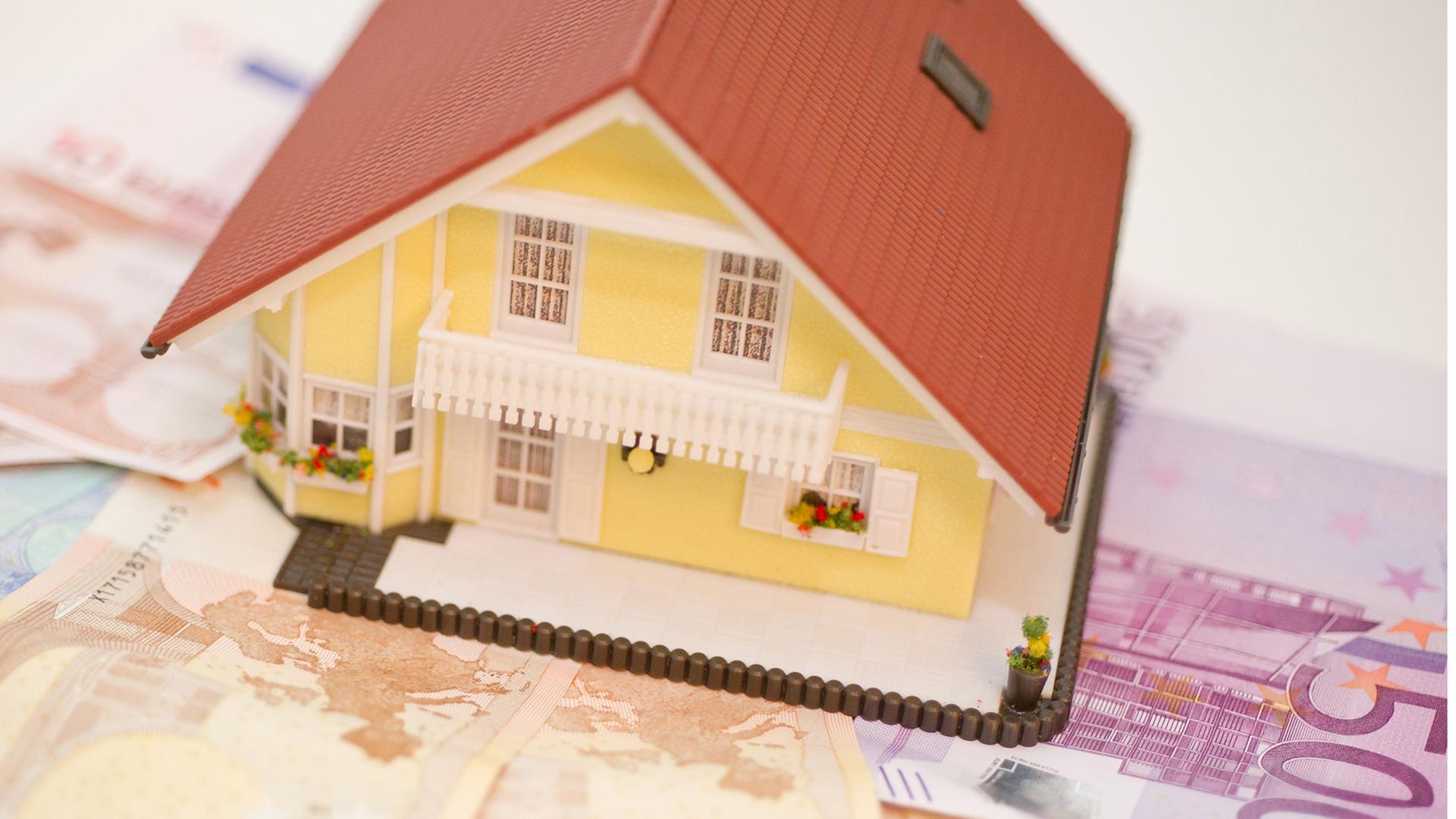 Ein Modellbauhaus steht neben einem Geldschein.