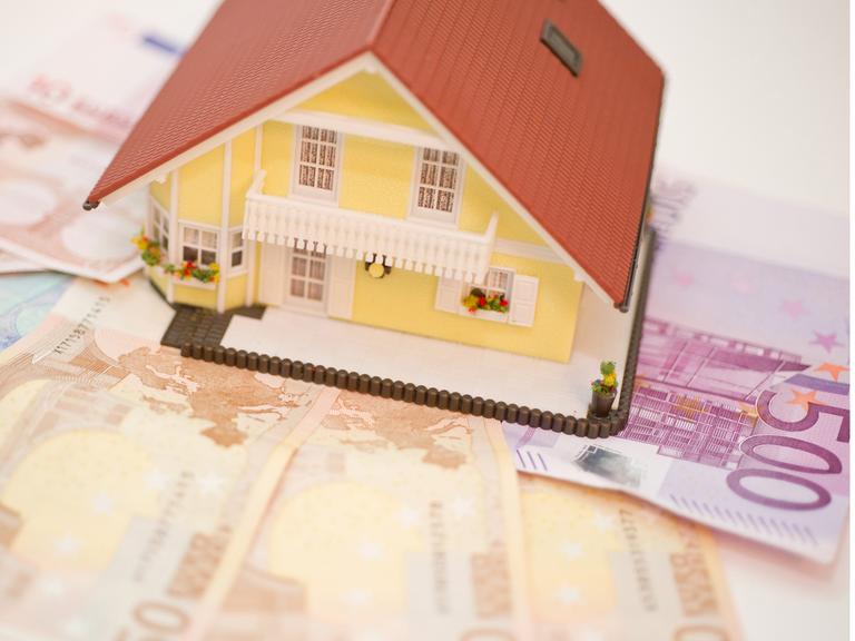 Ein Haus steht auf Geldscheinen. Symbolbild für Haus und seine Kosten