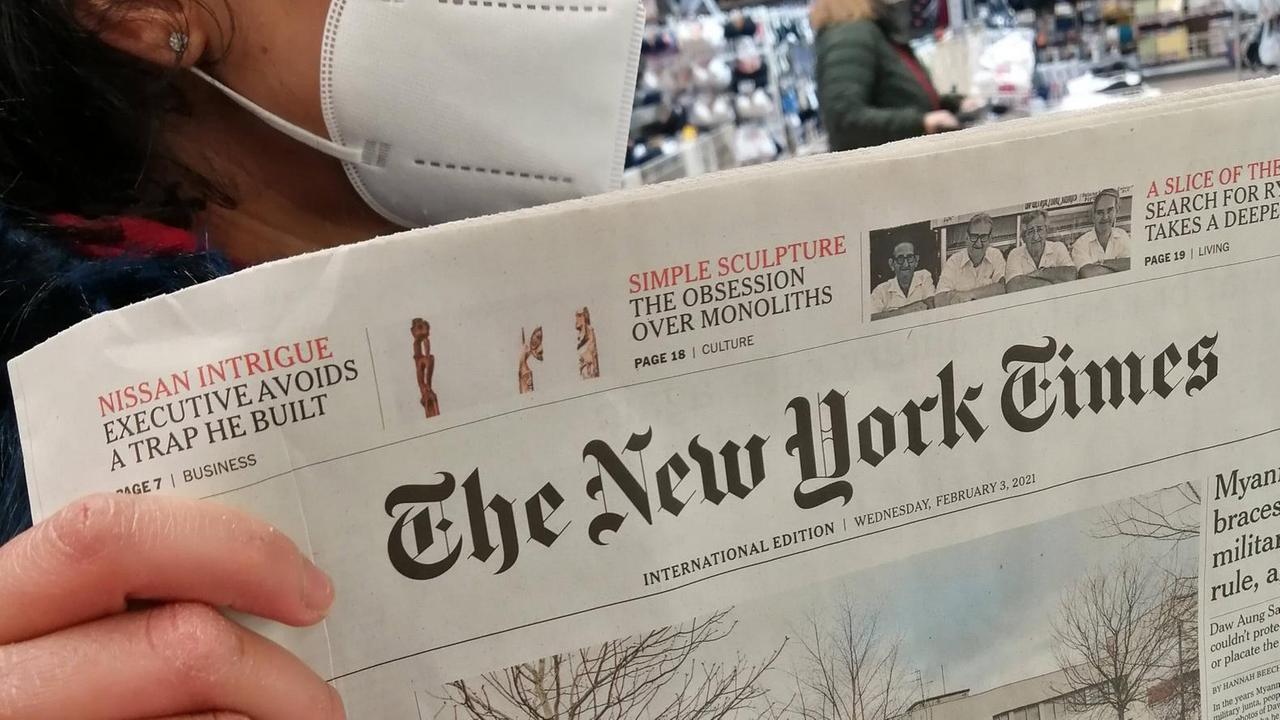 Eine Frau mit FFP2-Maske hält eine Printausgabe der "New York Times" in der Hand