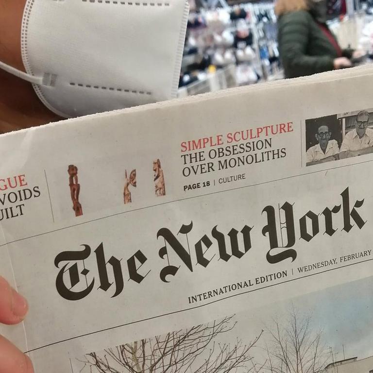 Eine Frau mit FFP2-Maske hält eine Printausgabe der "New York Times" in der Hand