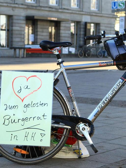 Auf einem Fahrrad ist ein Zettel angebracht, der einen gelosten Bürgerrat in Hamburg fordert.