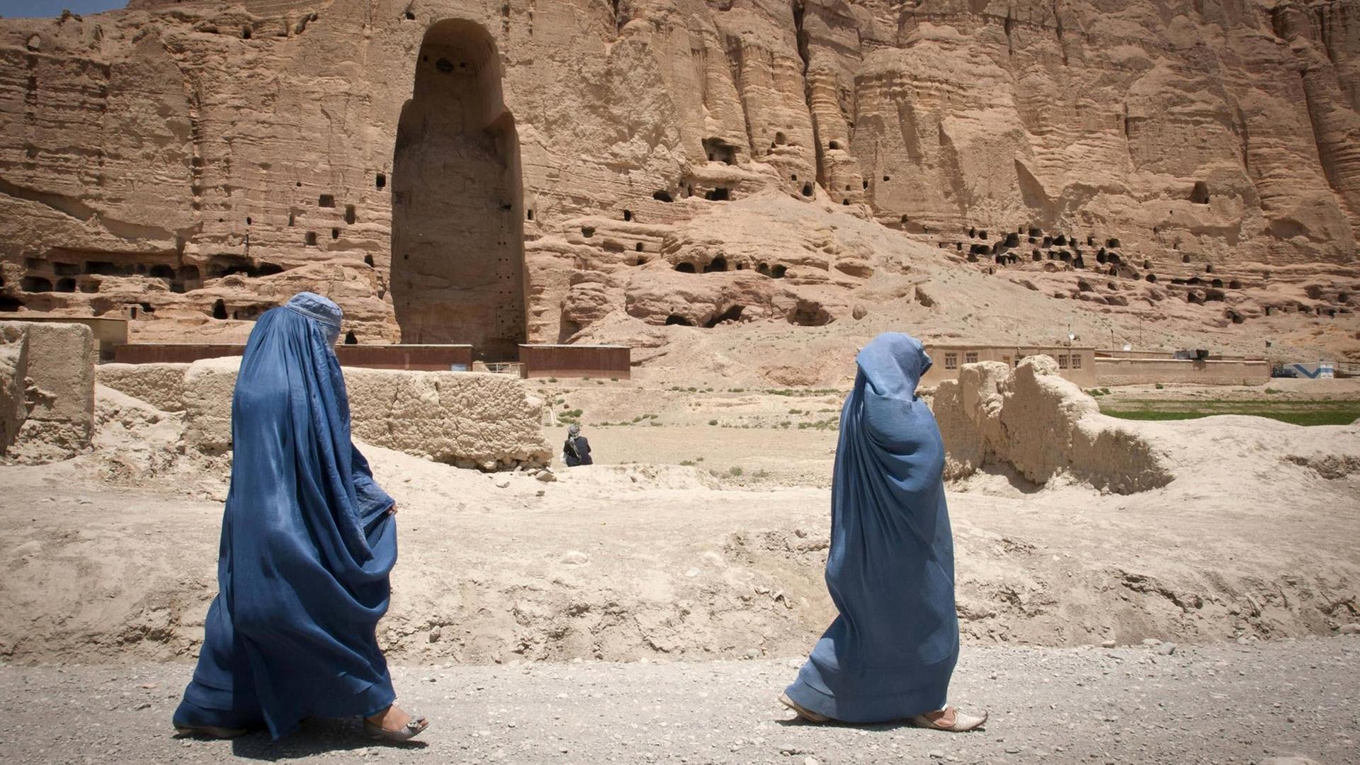 Zwei Frauen, die Burka tragen, laufen an der riesigen Lücke vorbei, wo einst eine der antiken Buddha-Statuen von Bamiyan stand. Afghanistan, 17.06.2012