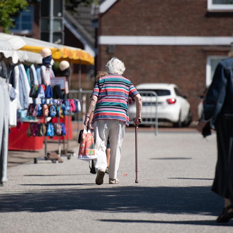 Eine ältere Frau geht über den Wochenmarkt.