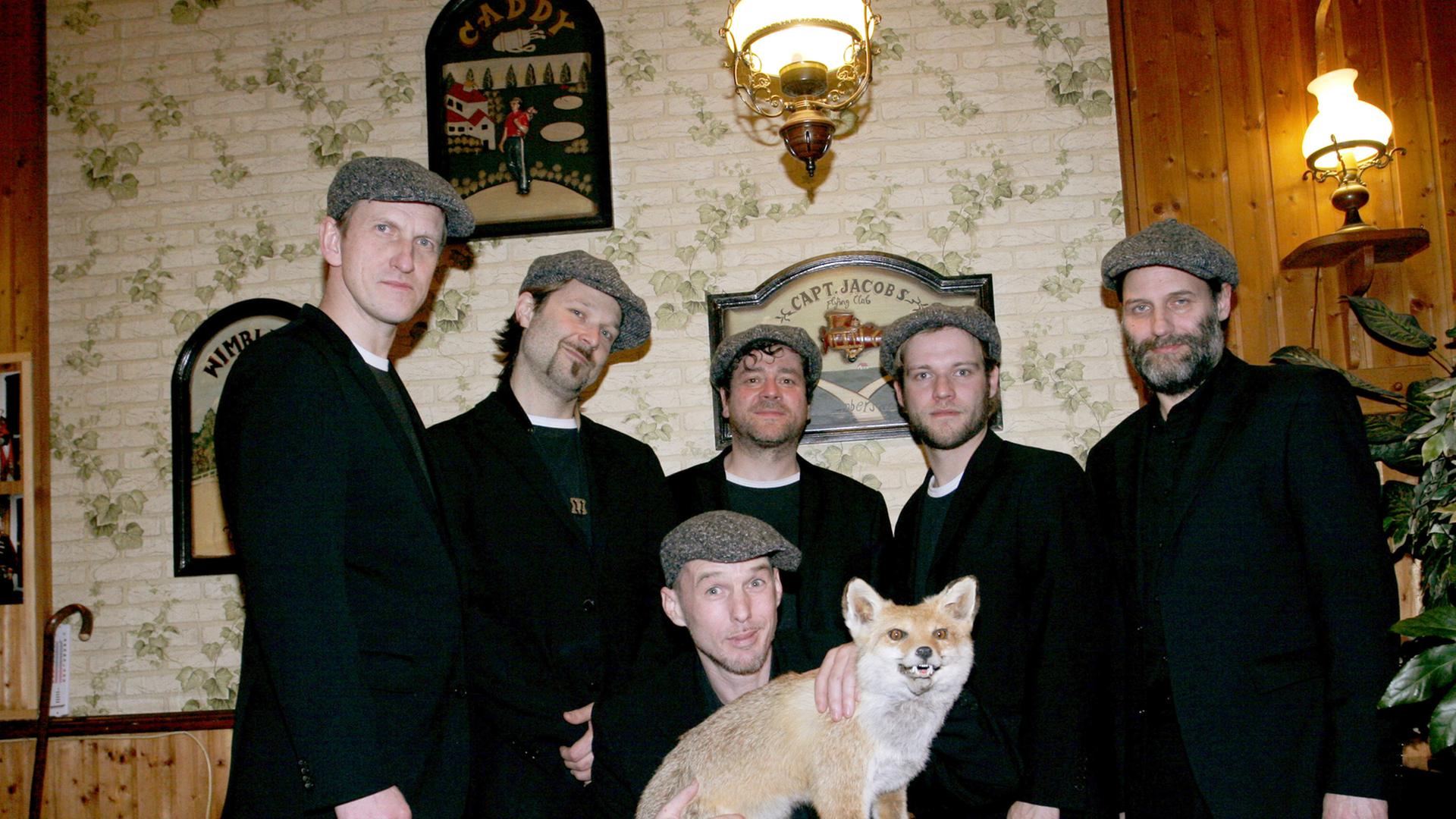 Die Mitglieder der Band "Jazzkantine" stehen zusammen in schwarzen Anzügen. Einer kniet in der Mitte und hält einen ausgestopften Wolf in den Händen. 