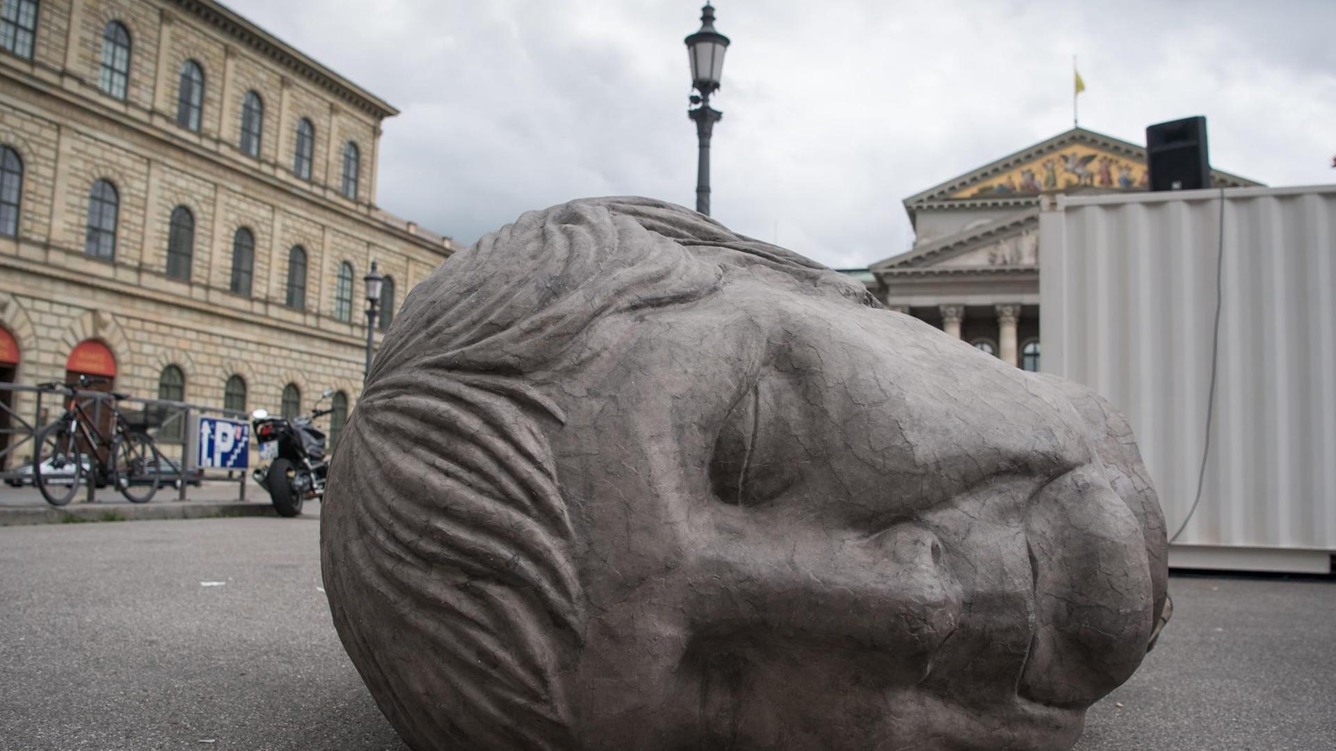 Ein grauer Pappkopf, der die deutsche Bundeskanzlerin Angela Merkel darstellen soll, liegt am 31.05.2016 in München (Bayern) auf dem Gehweg vor der bayerischen Staatsoper. Die Skulptur gehört zur Perfomance "Die Irrenden.