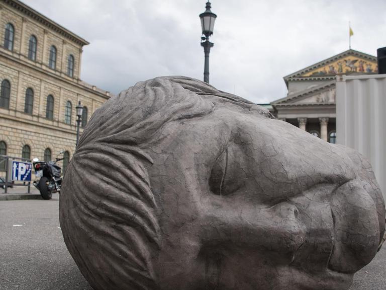Ein grauer Pappkopf, der die deutsche Bundeskanzlerin Angela Merkel darstellen soll, liegt am 31.05.2016 in München (Bayern) auf dem Gehweg vor der bayerischen Staatsoper. Die Skulptur gehört zur Perfomance "Die Irrenden.