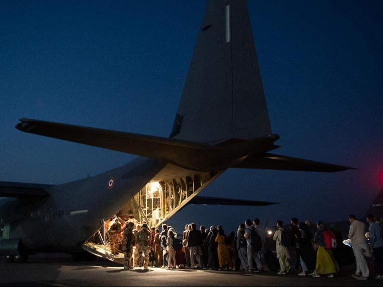 Auf einem nächtlichen Rollfeld stehen Menschen Schlange, um einen Airbus zu besteigen.