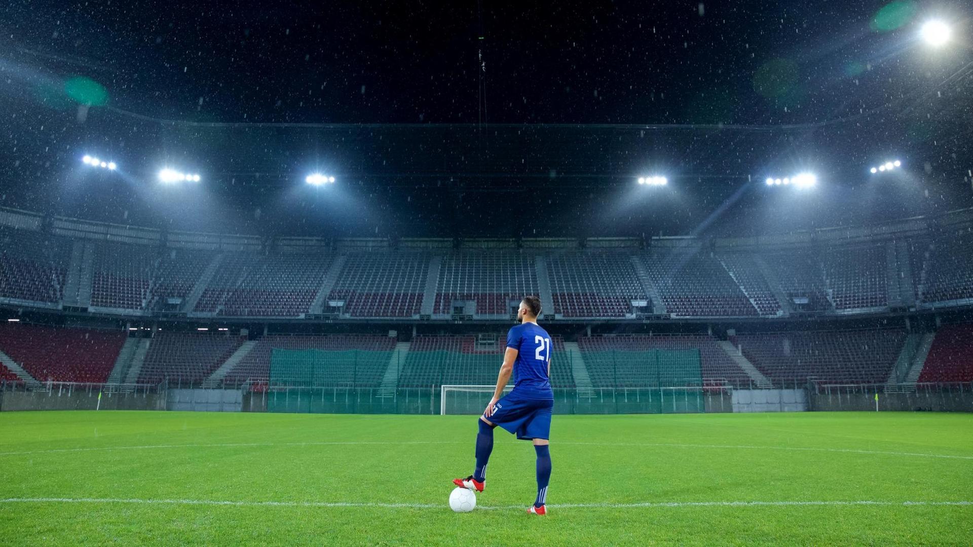 Ein Fussballspieler steht alleine in einem Stadium ohne Publikum.