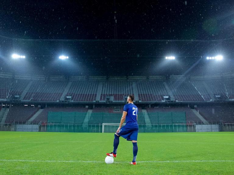 Ein Fussballspieler steht alleine in einem Stadium ohne Publikum.