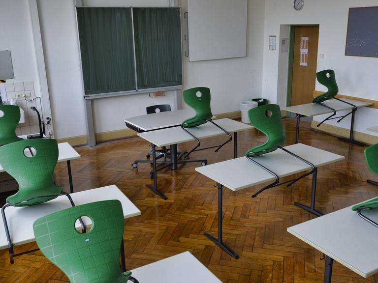 Ein leeres Klassen-Zimmer mit Tischen und hochgestellten Stühlen. 