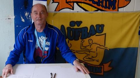 Andreas Steinhoff sitzt an einem Tisch, an der Wand hinter ihm hängt ein Banner seines Vereins