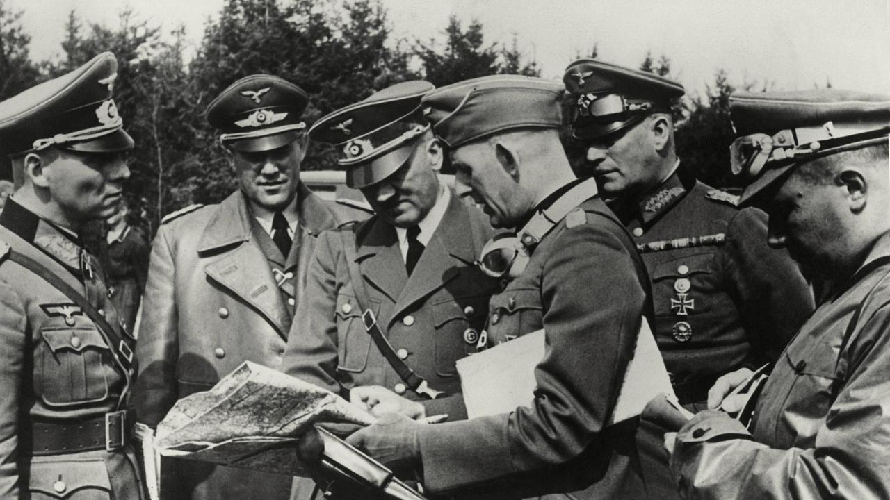 Das Schwarz-weiß-Pressebild von 1939 zeigt Adolf Hitler im Halbkreis mit Erwin Rommel, Karl-Heinrich Bodenschatz, Rudolf Schmundt, Wilhelm Keitel und Albert Bormann. Alle sind in Uniform und haben die Köpfe über eine Landkarte gebeugt. 