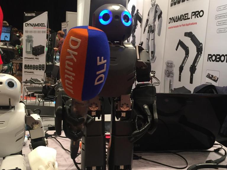 Zwei Roboter, fotografiert auf der Roboter Messe Hamburg. Einer hält ein Mikrofon in der Hand.