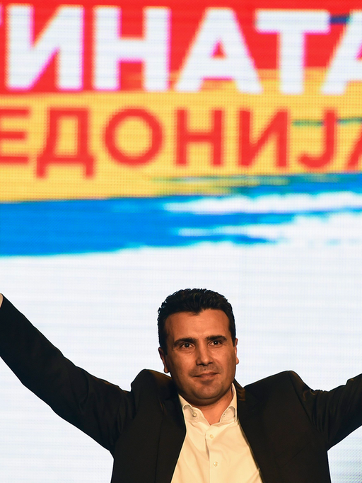 Zaef am 10. März 2015 in Skopje bei einer Rede auf einer Volksversammlung vor einem bunten Plakat. Um seine Worte zu betonen, hebt er beide Arme.