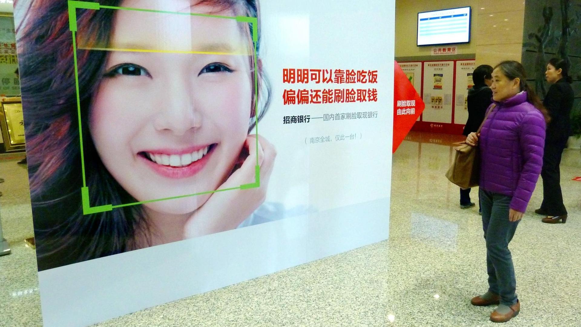 Eine Frau schaut in Nanjing in der Provinz Jiangsu auf ein Werbeplakat, das für das Geldabheben am Automaten per Gesichtserkennung wirbt