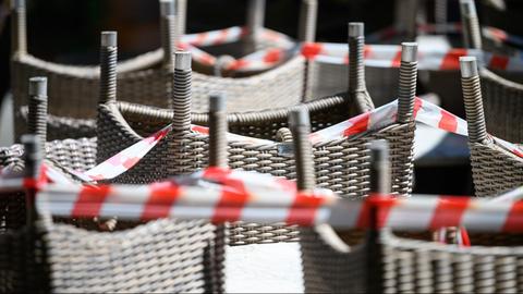 Gestapelte Stühle eines Restaurants sind mit Absperrband umgeben.