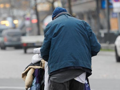 Eine obdachloser Mann läuft mit einem Einkaufswagen mit Jacken und Decken am Zoologischen Garten über die Straßen.