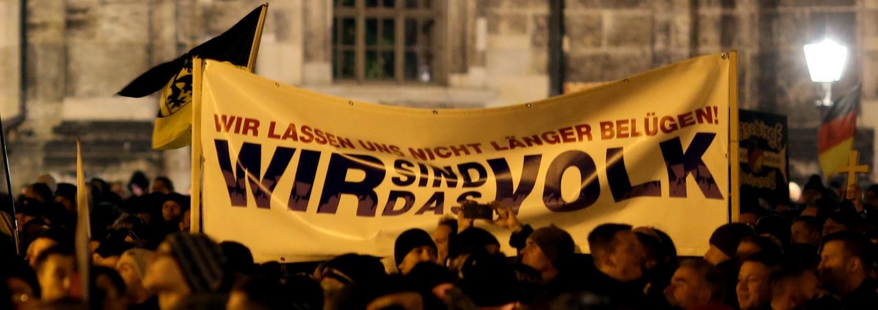 Pegida-Demonstranten halten ein Tranparent hoch, auf dem "Wir sind das Volk" steht.
