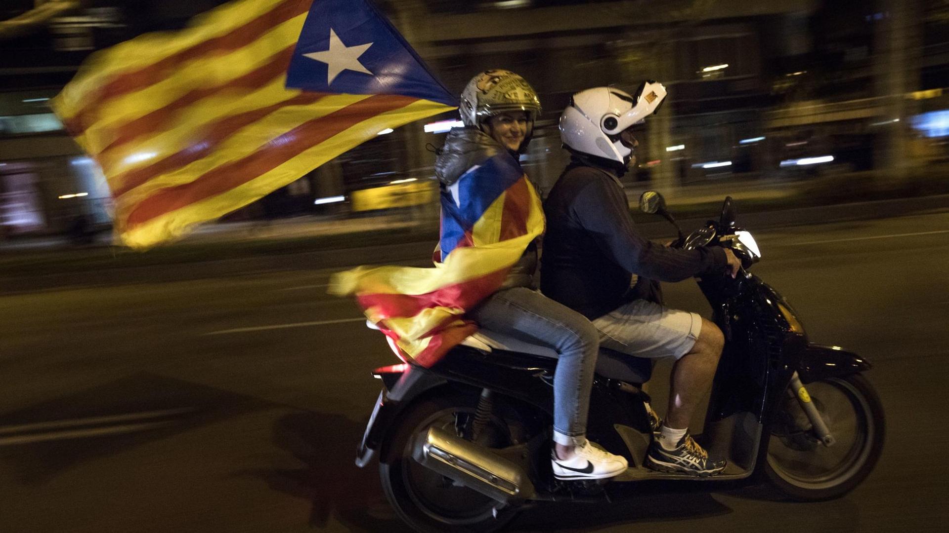 Dine Frau schwenkt die Flagge der katalanische Nationalisten "Estelada blava" auf einem Motorrad.