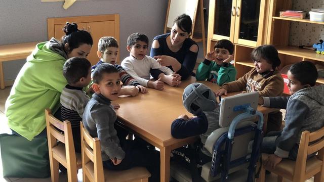 Zu sehen sind palästinensische Kinder und 2 Erwachsene an einem Tisch.