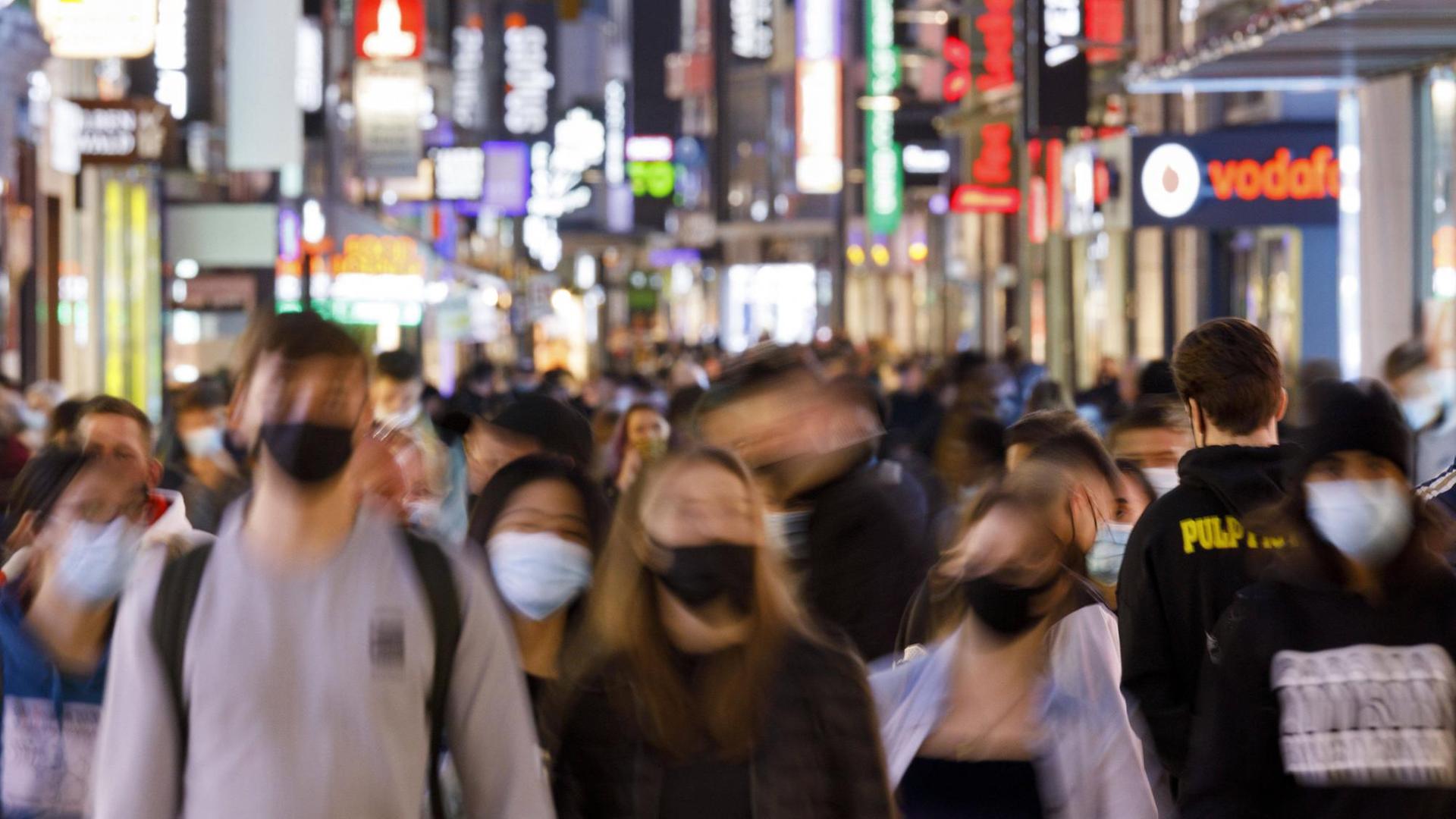 Menschen gehen mit Masken durch eine Fußgänger-Zone. 