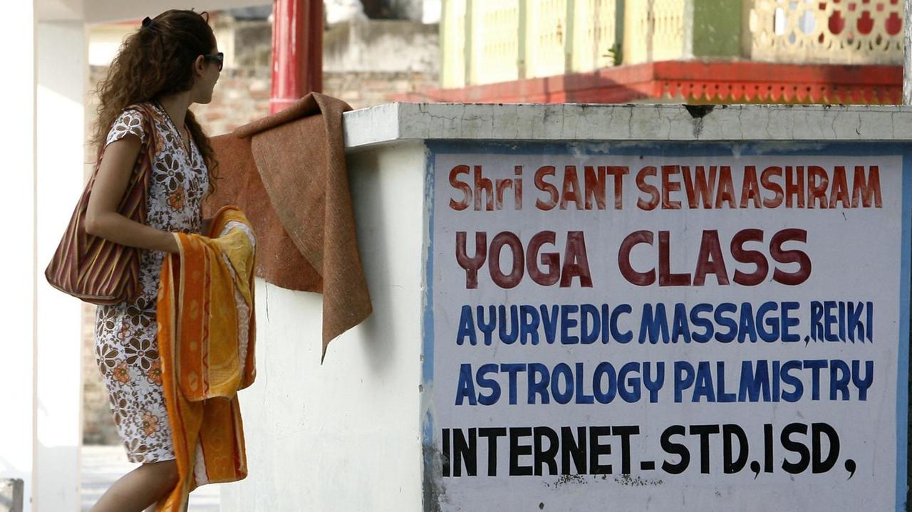 Touristen vor einer Inschrift, die für Yoga-Kurse wirbt, im indischen Rishikesh.
