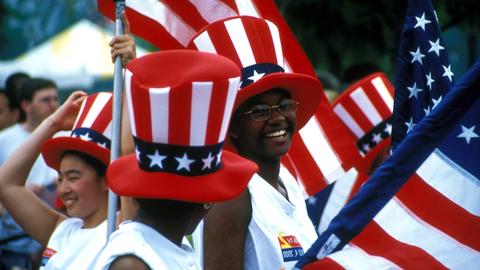 Menschen jubeln mit Stars-and-Stripes-Zylindern und Nationalflaggen - Begeisterung und laute Verurteilung der USA liegen oft dicht beieinander