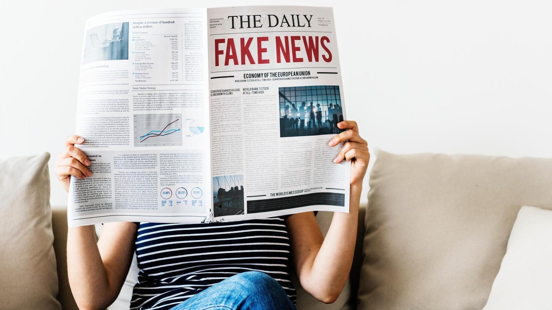 Eine Frau sitzt auf einem Sofa und liest die Zeitung "The Daily Fake News".