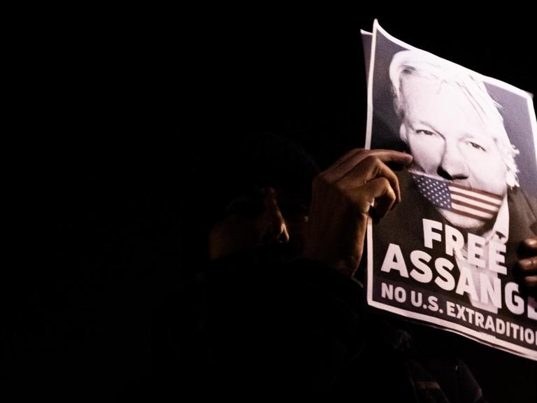 Protestierende in Paris am 05.11.2019 beim "Million Mask March" halten ein Schild von Julian Assange in die Höhe, auf dem er mit der amerikanischen Fahne geknebelt ist.